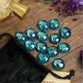 Blue glass witch stones with star patterns on a wooden surface next to a black drawstring bag.