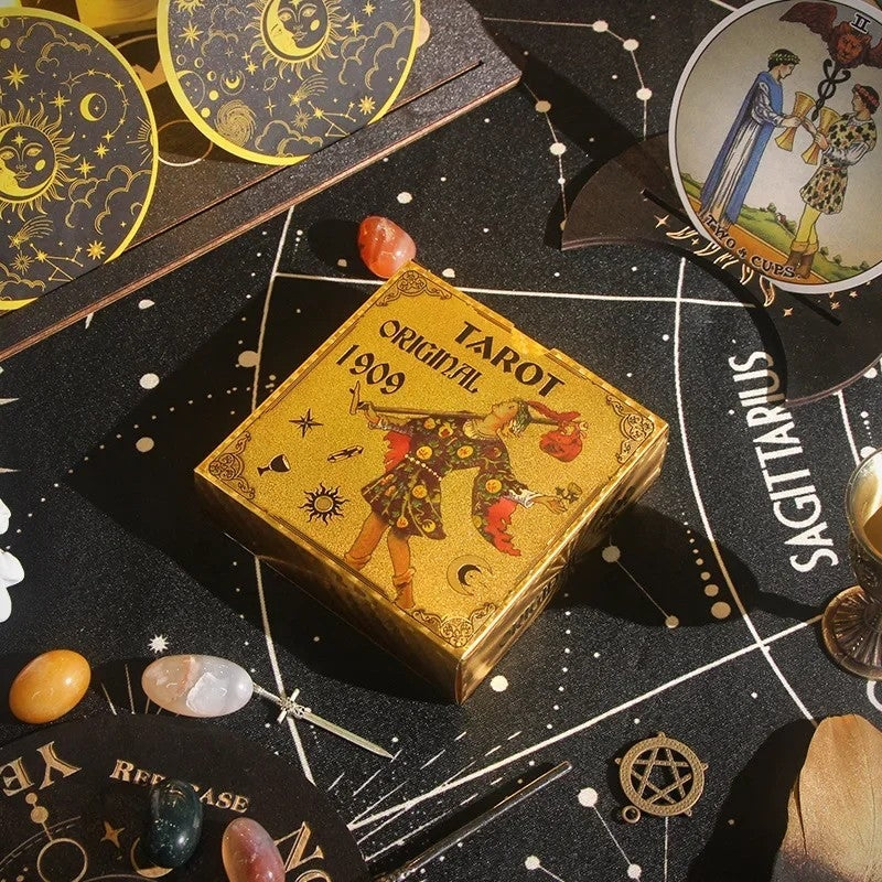 Gold tarot card box on a black tarot board with cards and crystals.