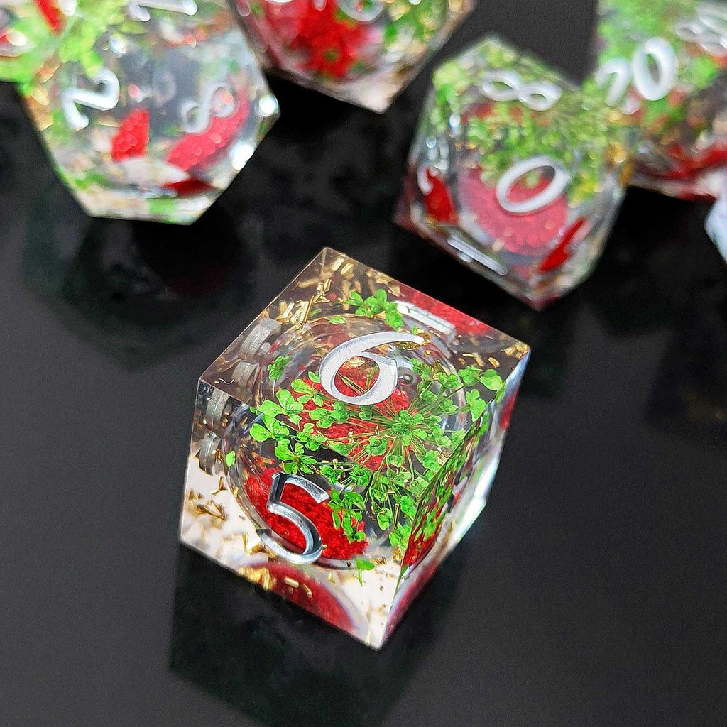 Close-up of a transparent botanical resin liquid sand core dice with red, green, and gold numbers on a black background