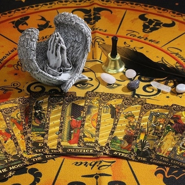 Tarot cards with angel statue, candles, and feather on a tarot tablecloth.