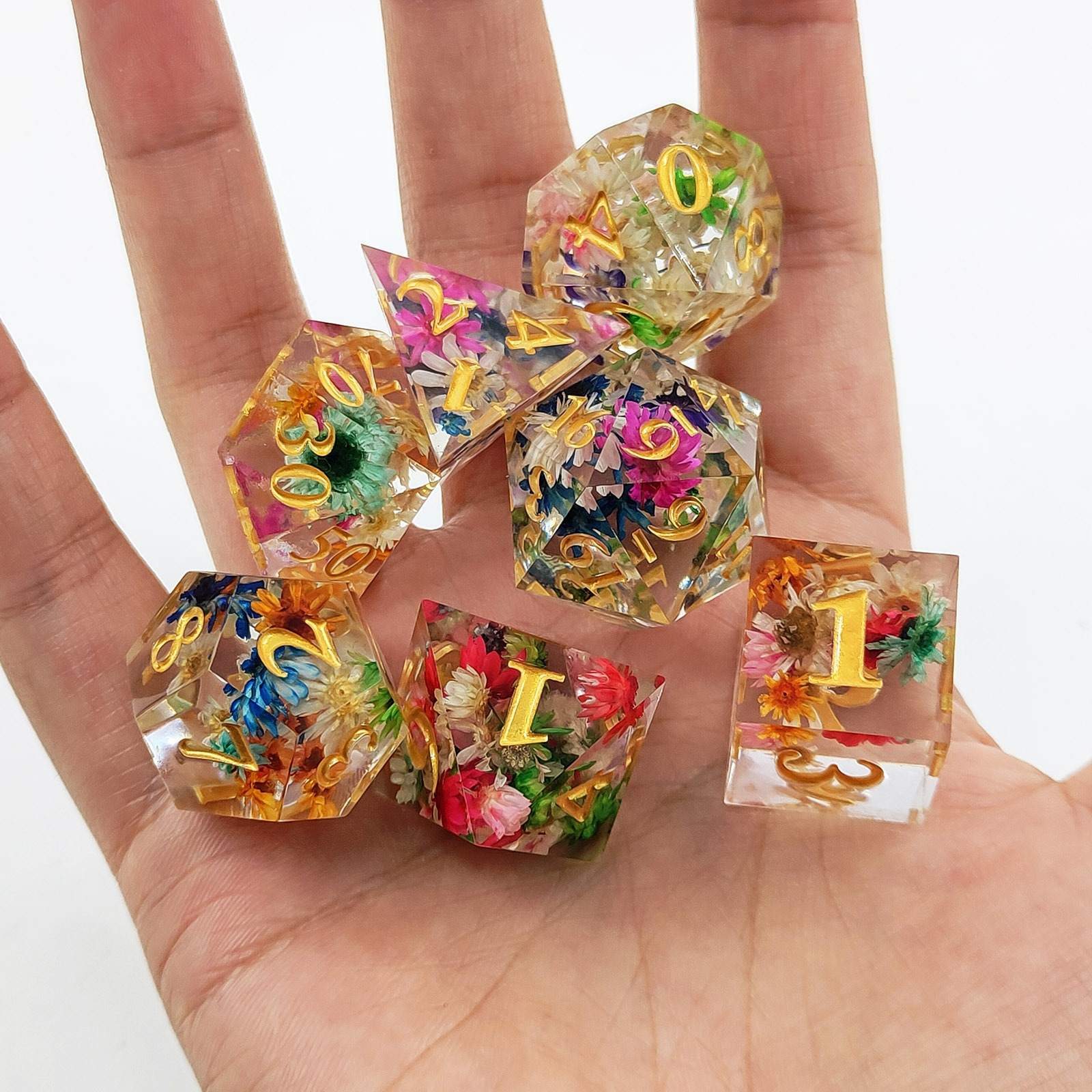 Colorful Sharp Edge Polyhedral resin dice with floral designs held in a hand against a white background