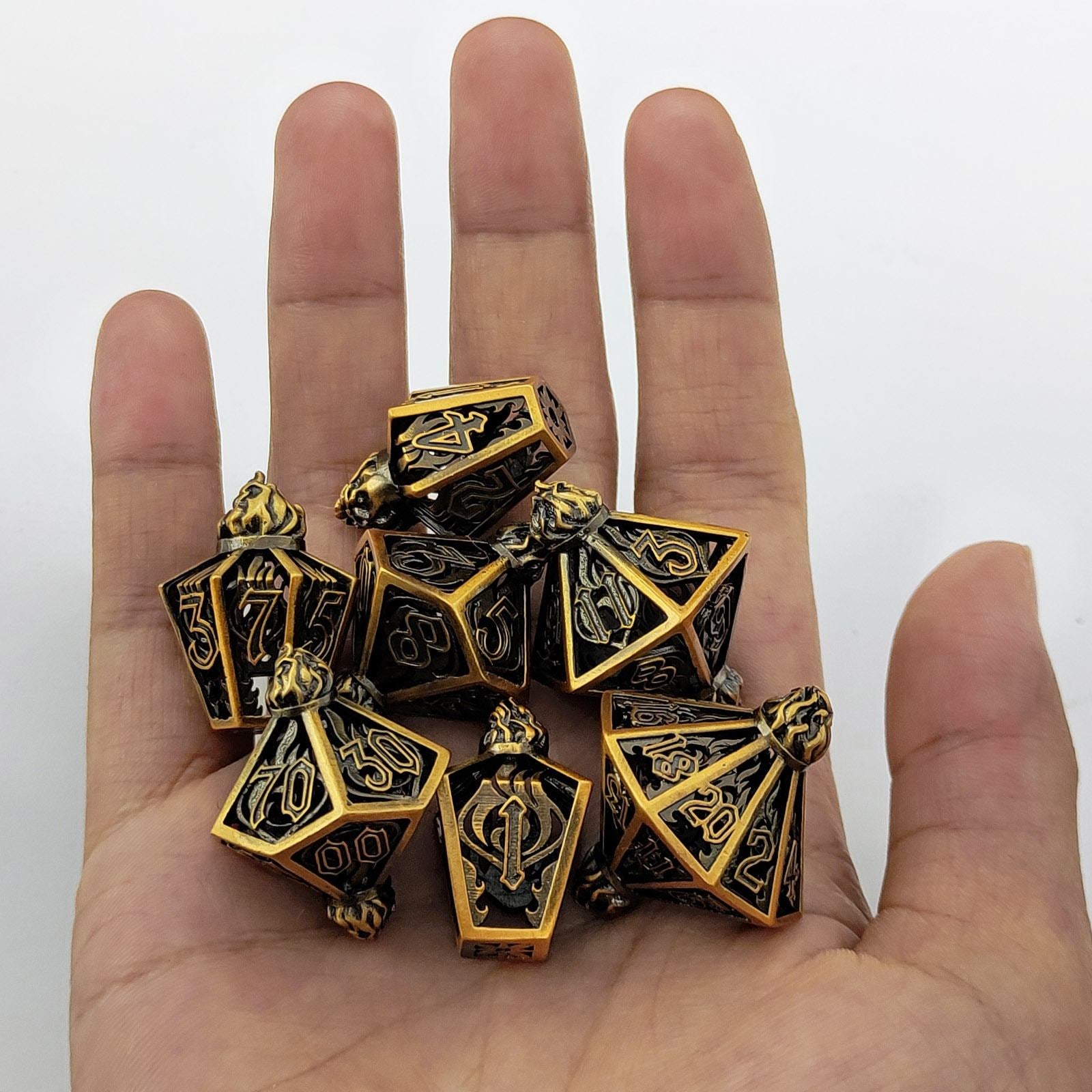 Gold and black polyhedral metal holow dice set held in a hand against a white background