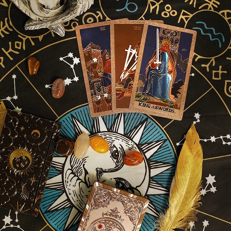 foil Tarot cards on a mystical background with celestial symbols and a candle.