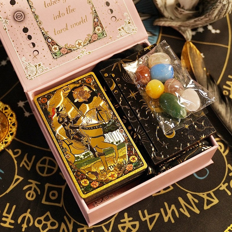 Goild foil Tarot cards with a pink box and colorful Chakra stones on a black background with astrological symbols.
