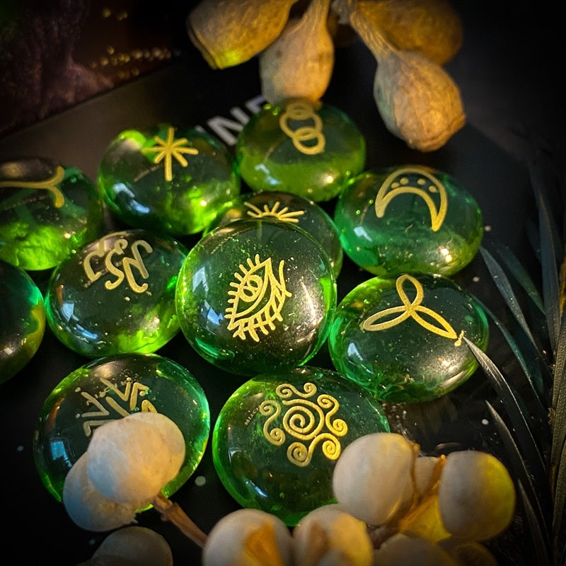 Green glass rune stone with gold symbols on a dark surface with flowers.