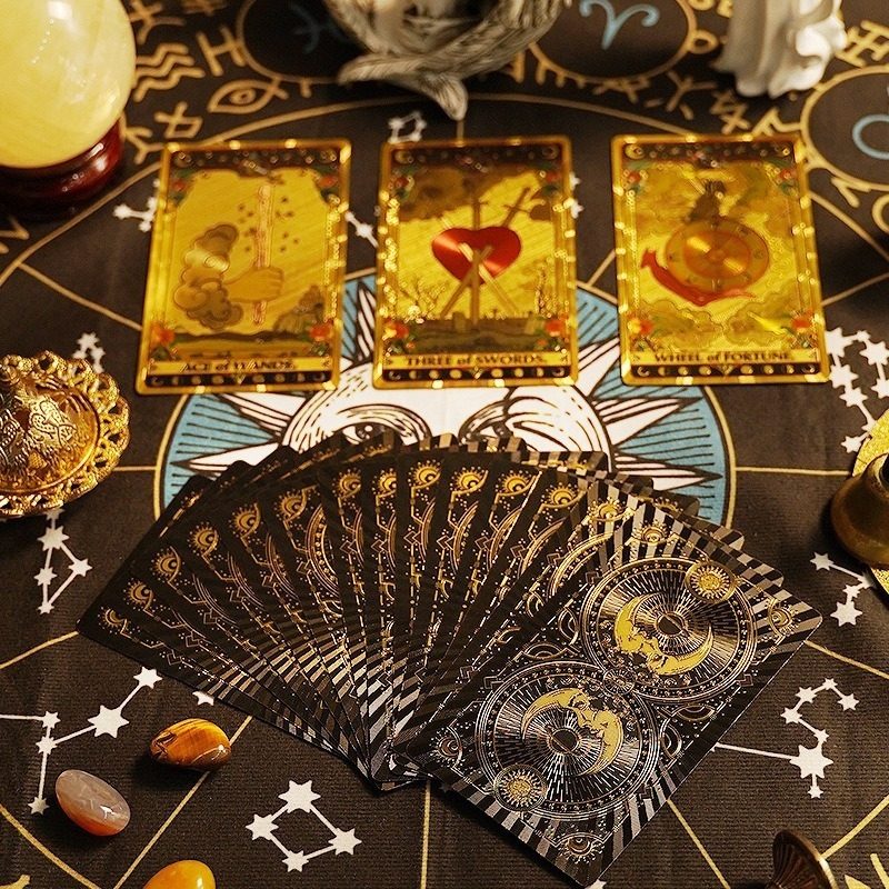 Collection of premium gold foil tarot cards on a mystical table with astrological symbols and crystals.
