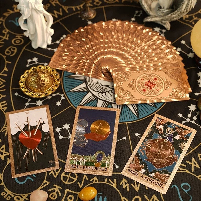 Gold tarot cards fanned out on a black astrological table with three cards displayed.