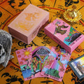 Pink tarot card deck with tarot cards and decorative items on a yellow background with astrological signs.