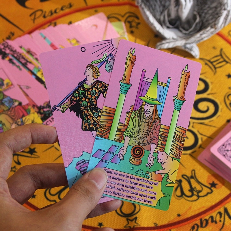 Colorful tarot card held by a hand on a tarot table with other cards in the background.
