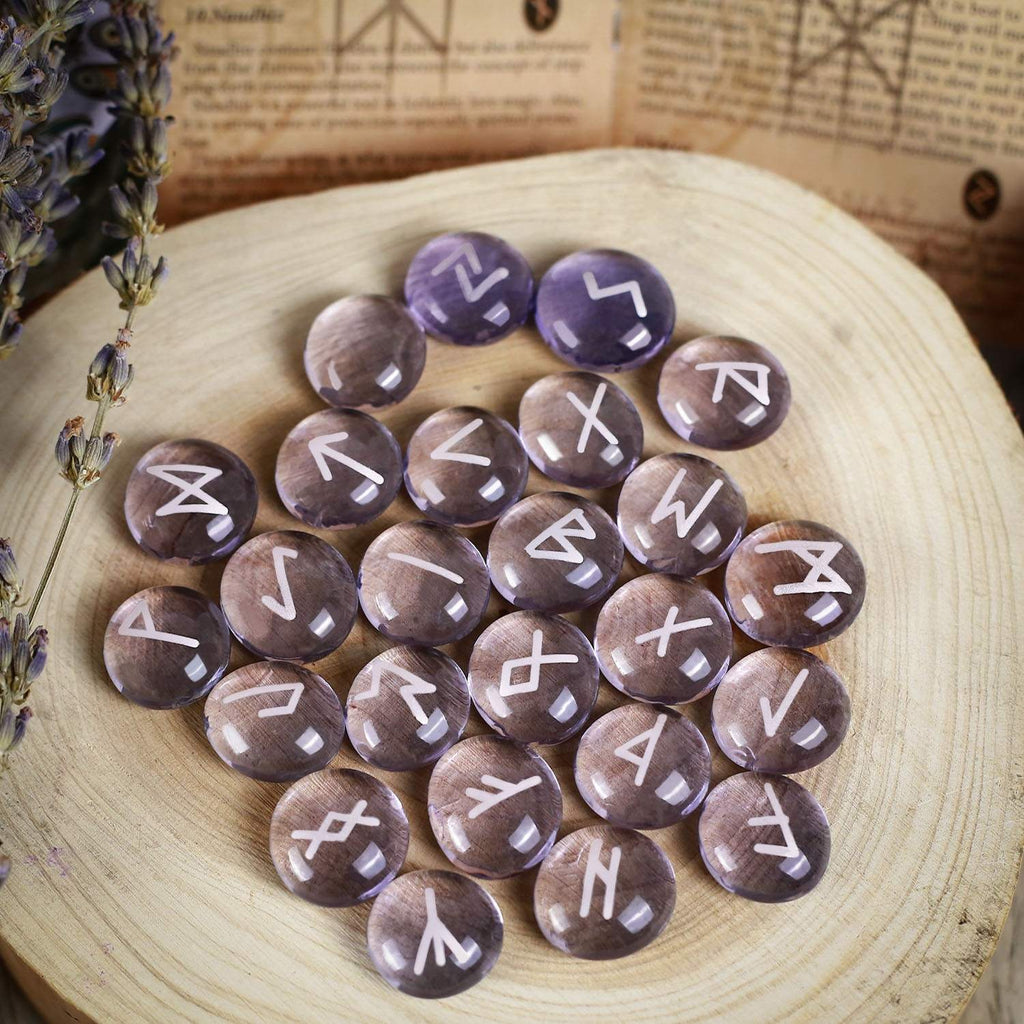 Runes stones with white symbols on a wooden surface with lavender and an open book in the background