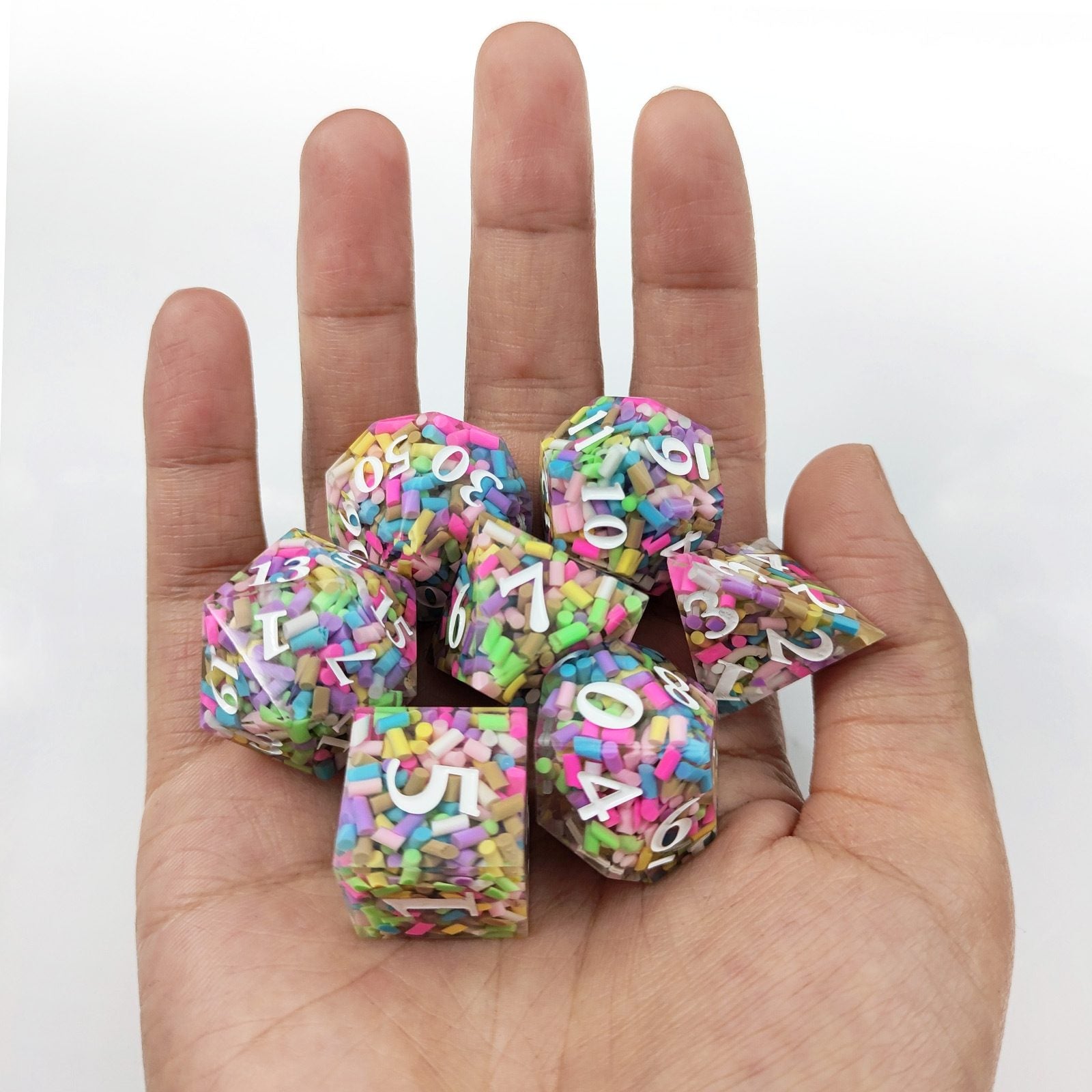 Colorful polyhedral resin dice with letter and number patterns held in a hand against a white background