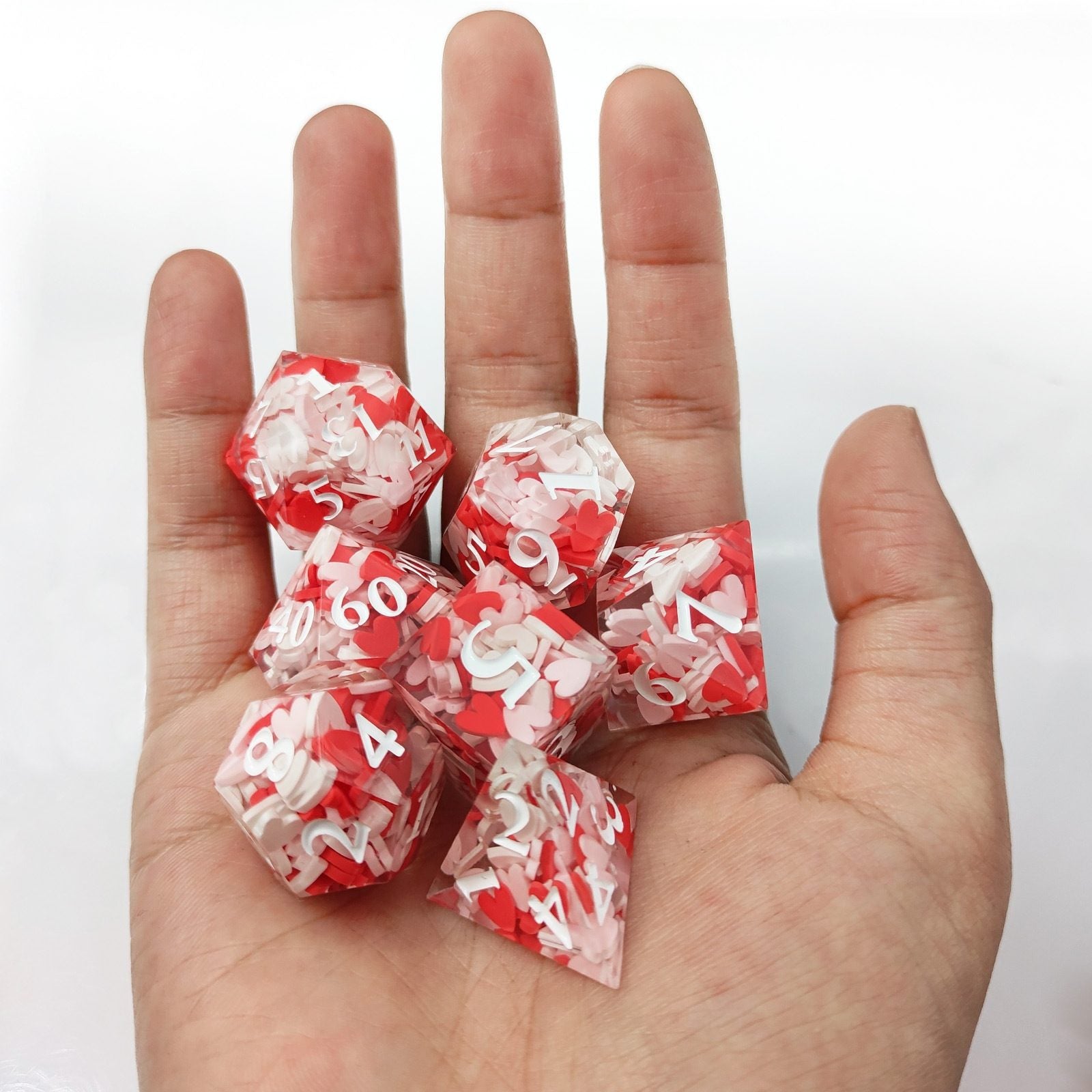 Hand holding red and white Sharp Edge Polyhedral resin dice with numbers on a white background