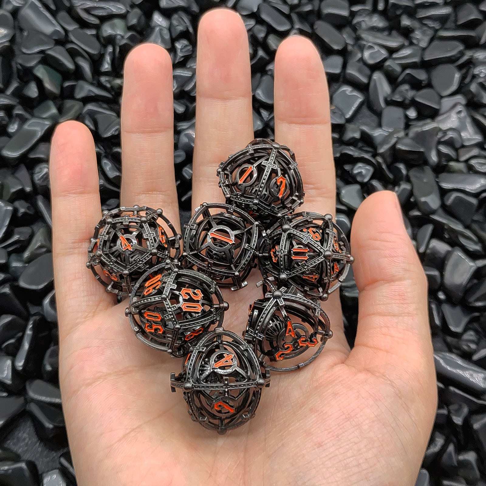 Hand holding metallic Hollow Metal Orb Chime DND dice with black and orange design against a dark textured background