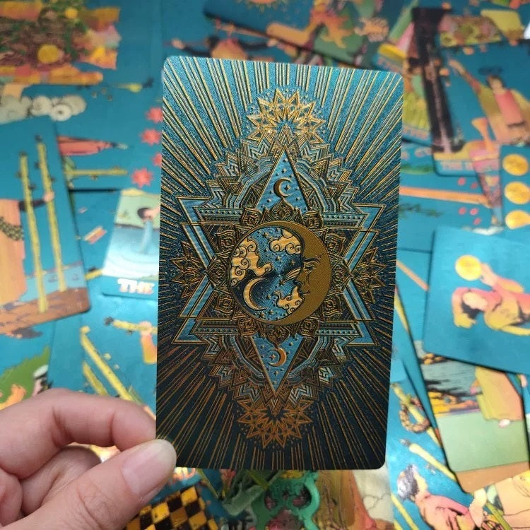 Teal Foil tarot card with sun and moon design held over a colorful array of tarot cards.